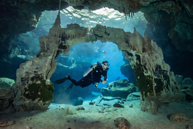 Scuba diver swimming through underwater cave arch in Malta